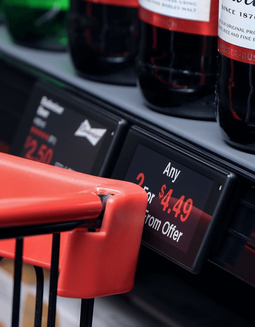 A shopping cart handle beside black-framed shelf labels showing a multi-buy offer